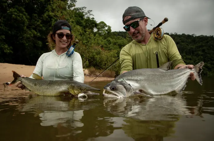 Two anglers holding large fish in the shallows