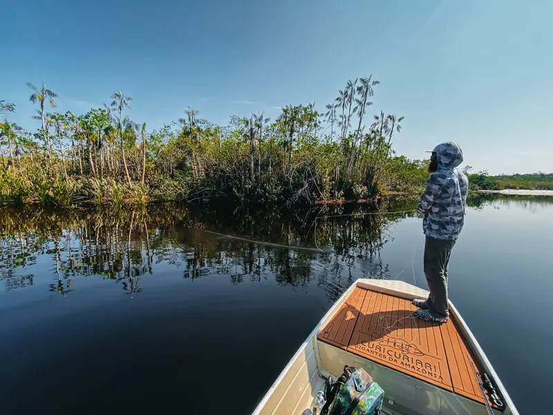 An angler casting from the bow of a boat on a calm lagoon